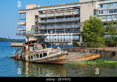 Dnipro, Ukraine - September 04, 2019: Semi-flooded river pleasure boat at an abandoned pier on background of dilapidated river station Stock Photo