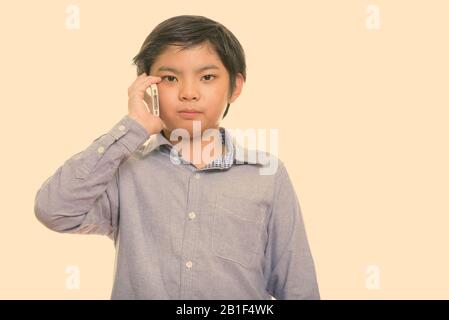 Studio shot of cute Japanese boy talking on mobile phone Stock Photo