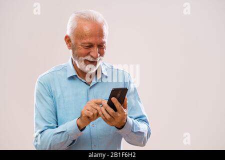 Portrait of cheerful senior man who is using smartphone. Stock Photo