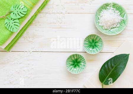 Green plant leaf, aromatic sea salt and towels. Concept for spa, beauty and health salons. Close up photo on white wooden background, top view Stock Photo