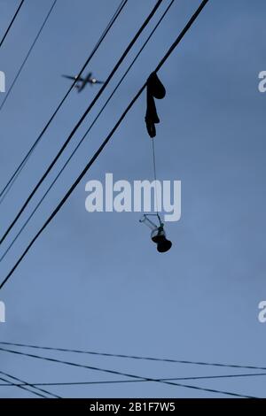 A clear glass Bong tied to a sock hanging from overhead power lines, as a small toy like plane flies in the blue evening sky over, Newtown, Australia Stock Photo