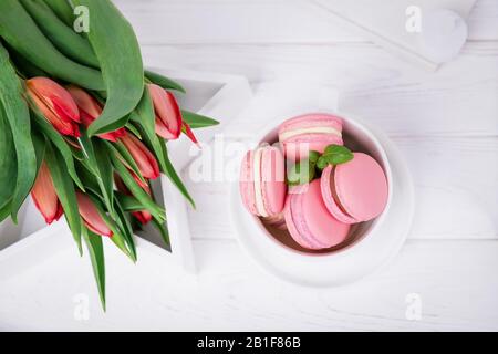 Homemade french dessert pink macaroons or macarons and spring tulips on white background, copy space Stock Photo