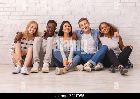 Happy students posing over white brick wall Stock Photo