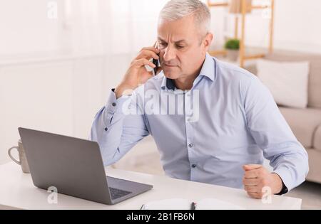 Serious mature man talking on mobile phone at office Stock Photo