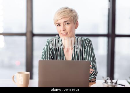 Businesswoman Smiling To Camera Sitting At Work In Modern Office Stock Photo