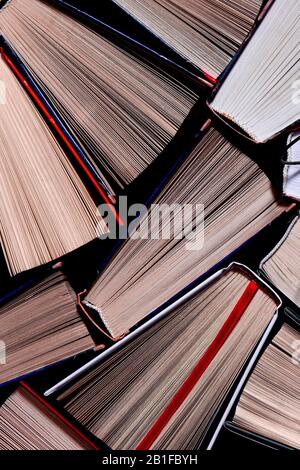 Many open multicolored books stand on the shelf next to old round glasses Stock Photo