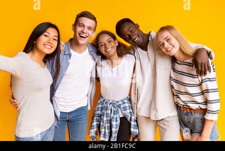 Friendly international group of teenagers taking selfie over yellow background Stock Photo