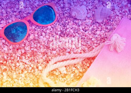 Beach scene. Sunglasses and beach bag lying on the sea coquina shells. Gradient color Stock Photo