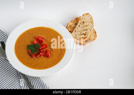 Vegetable soup with lentils on a white background. Served with chopped cherry tomatoes and herbs. Nearby are pieces of ciabatta. Raw groats in the bac Stock Photo