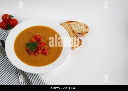 Vegetable soup with lentils on a white background. Served with chopped cherry tomatoes and herbs. Nearby are pieces of ciabatta. Raw groats in the bac Stock Photo