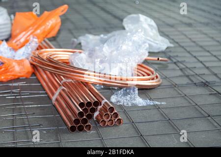Close-up skein of new shiny copper pipes on floor, plastic package, lay pipeline, installation tubes on floor with warm heating of apartment, view fro Stock Photo