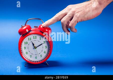 Red alarm clock on the color background. A hand of person switching off an alarm clock in the morning Stock Photo