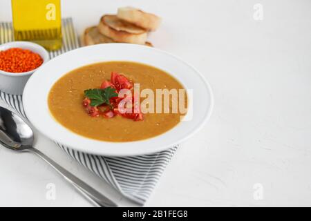 Vegetable soup with lentils on a white background. Served with chopped cherry tomatoes and herbs. Nearby are pieces of ciabatta. Raw groats in the bac Stock Photo