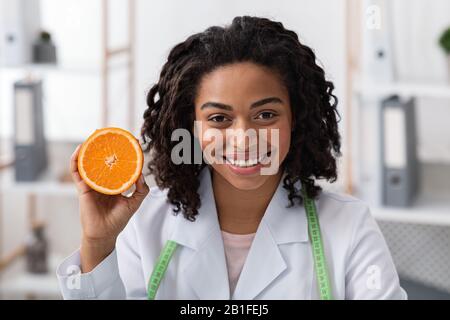 Close up portrait of female doctor holding orange half Stock Photo