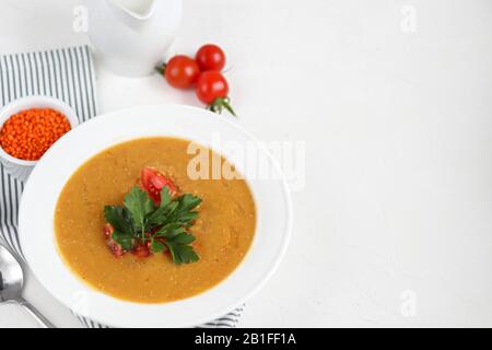 Vegetable soup with lentils on a white background. Served with chopped cherry tomatoes and herbs. Nearby are pieces of ciabatta. Raw groats in the bac Stock Photo