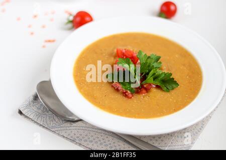 Vegetable soup with lentils on a white background. Served with chopped cherry tomatoes and herbs. Nearby are pieces of ciabatta. Raw groats in the bac Stock Photo