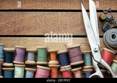 Vintage wooden spools of multicolored threads, tailoring scissors, thimbles, measuring tape. Sewing items, view from above. Stock Photo