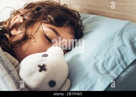 detail of an adorable little girl sleeping in bed hugging her teddy bear, happy childhood and healthy rest concept Stock Photo