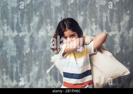 portrait of a funny little girl about to throwing a cushion and start a pillow war, home lifestyle concept and happy childhood, copy space for text Stock Photo