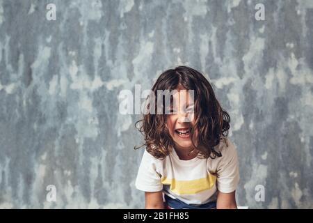 portrait of a happy little girl laughing out loud on a blue background, happy childhood and lifestyle concept, copy space for text