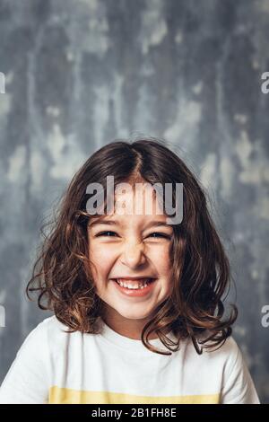 vertical portrait of a happy little girl smiling on a blue background, happy childhood and lifestyle concept, copy space for text Stock Photo