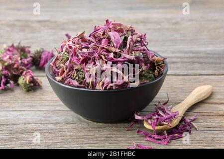 Healthy echinacea flowers in black ceramic bowl and dry coneflowers on wooden table. Herbal medicine. Stock Photo