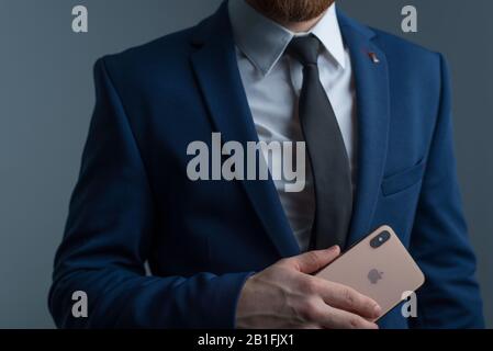 Zaporozhye. Ukraine. February 2020. Close-up portrait of a young bearded guy in a business suit holding an iPhone XS in his hand. New smartphone from Stock Photo