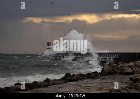 Dramatic stormy winter sunset at the Douro river mouth with big wave splash against north pier and beacon. Stock Photo