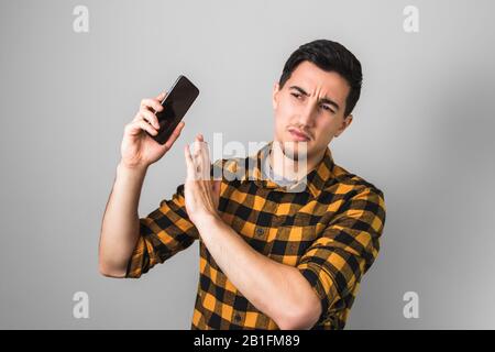 too much talk. young man in yellow shirt annoyed by a voice on phone, gesturing with one hand against on grey background Stock Photo