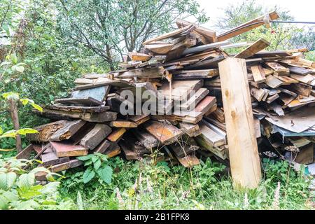 Pile of old rotten wooden planks with long rusty nails in garden against background of greenery after dismantling. Stock Photo