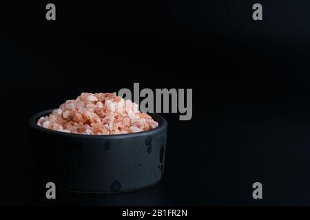 Pink Himalayan salt in black ceramic bowl. Black background, high resolution Stock Photo