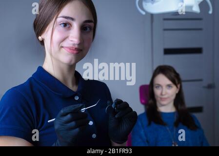 portrait of a young beautiful girl dentist doctor, in mask, smiling, holds dental instruments in his hand, on the background of the patient. At the de Stock Photo