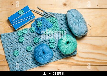 Composition of crocheted blue-green openwork napkins and equipment for knitting with copy space. Balls of yarn and plastic hooks on wooden background. Stock Photo