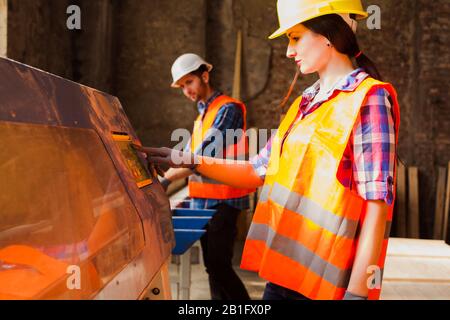 Workwoman in protected helmet and clothes pressing button on woodworking machine. Stock Photo