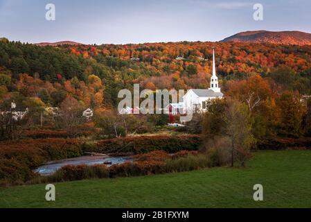 Stunning fall foliage and a traditional white wooden church in a mountain town at sunset
