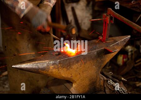 The blacksmith manually forging the molten metal on the anvil in smithy. Stock Photo