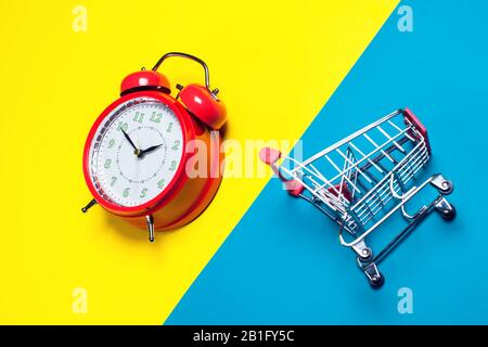 Red alarm clock, small shopping trolley on color background. Shopping concept Stock Photo