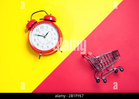 Red alarm clock, small shopping trolley on color background. Shopping concept Stock Photo