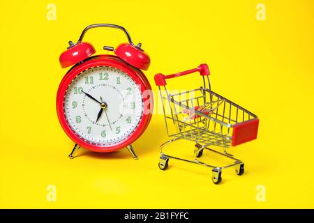 Red alarm clock, small shopping trolley on color background. Shopping concept Stock Photo