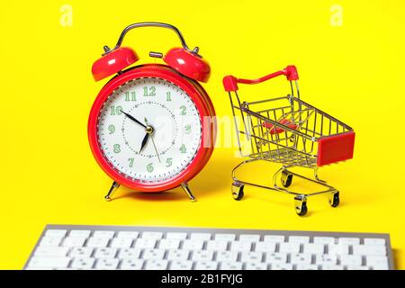 Red alarm clock, small shopping trolley, keyboard on color background. Online shopping concept Stock Photo