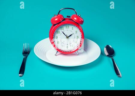 Red alarm clock on white plate on color background. Healthcare and food concept Stock Photo
