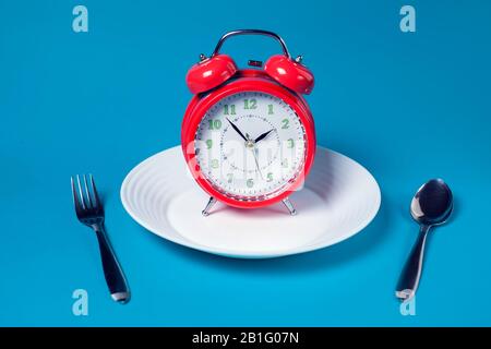 Red alarm clock on white plate on color background. Healthcare and food concept Stock Photo