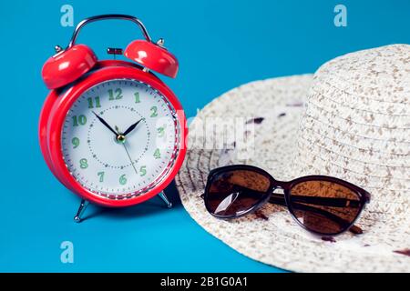 Red alarm clock, woman's hat and sunglasses on color background. Summer and vacation concept Stock Photo