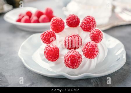 Delicious mini Pavlova meringue cake decorated with fresh raspberries, with a beautiful Cup lying on a platter. Stock Photo
