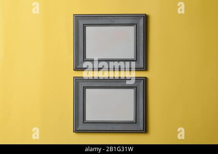 Two blank grey wooden photo frames hanging from a yellow wall Stock Photo