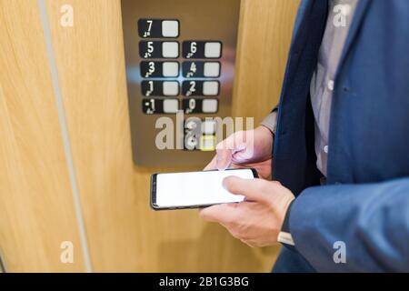 Businessman in elevator holding empty screen smartphone next to control panel. Stock Photo