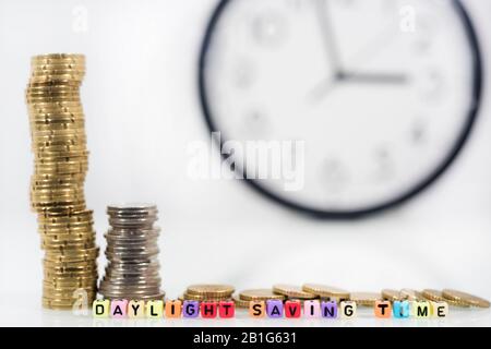 Coins with clock on white table. Summer Daylight Saving Time (DST). Turn time forward (+1h). Stock Photo