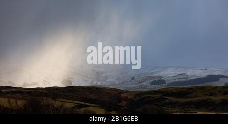 Near Tynygraig, Ceredigion, Wales, UK. 25th February 2020  UK Weather: A cold, breezy afternoon near Tynygraig in Ceredigion, as a small band of light breaks through the cloud, highlighting the snow forming on the Cambrian Mountains in Mid Wales this afternoon. © Ian Jones/Alamy Live News