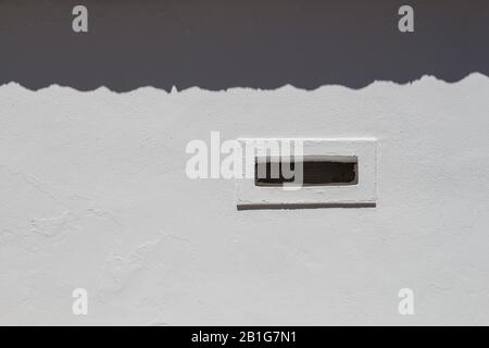 White facade of a building, enlightened by the sunlight. Shadow of the edge of a roof up. Ventilation gap with a white frame. Estoi, Portugal. Stock Photo