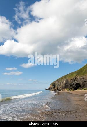 Colour photograph showing the wide expanse of the receding shallow tides  across the beach with cave and the sandy beach and the Penbryn seashore in C Stock Photo